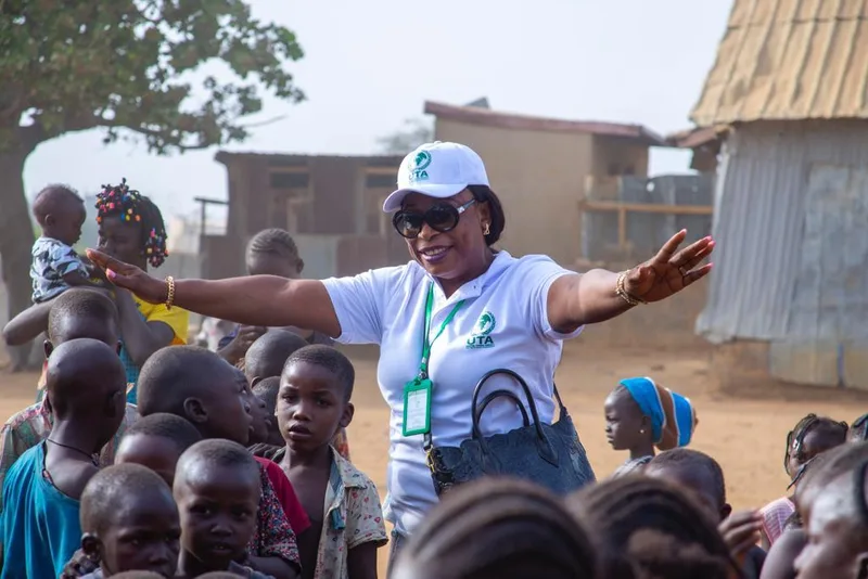 A UTA team member in a branded cap and shirt speaking with a group of children.